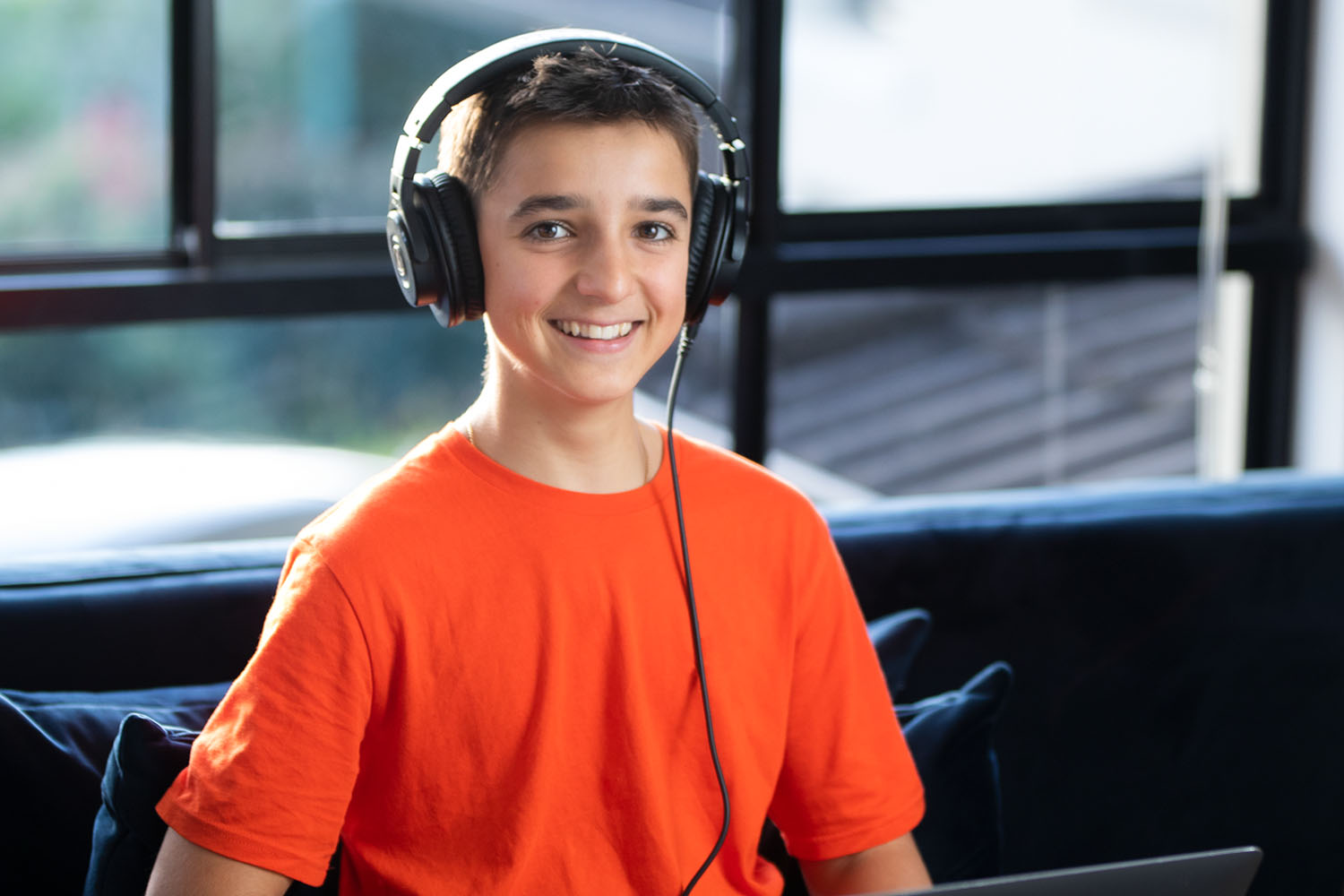 Super sweet teenage boy wearing headphones on a laptop smiling at camera