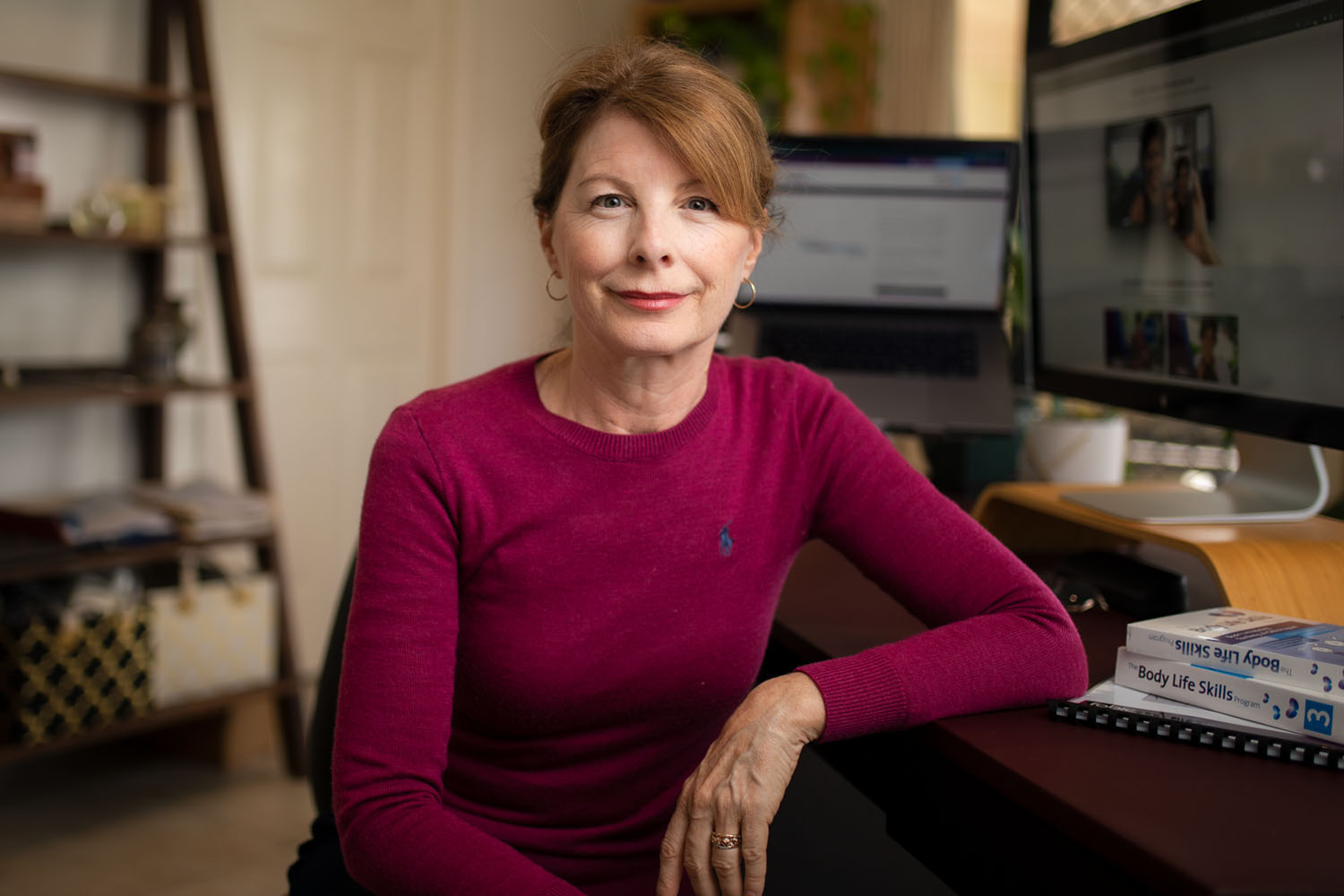 Woman with red hair sitting at desk looking at camera